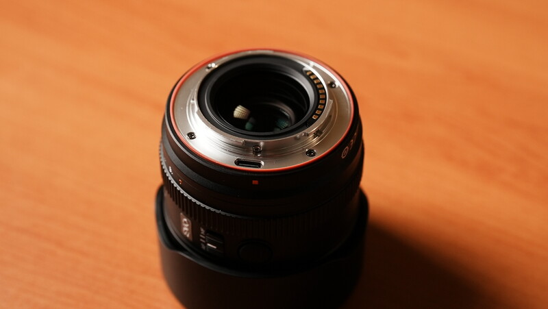 Telephoto zoom lens rear view on orange surface showing mount and glass elements