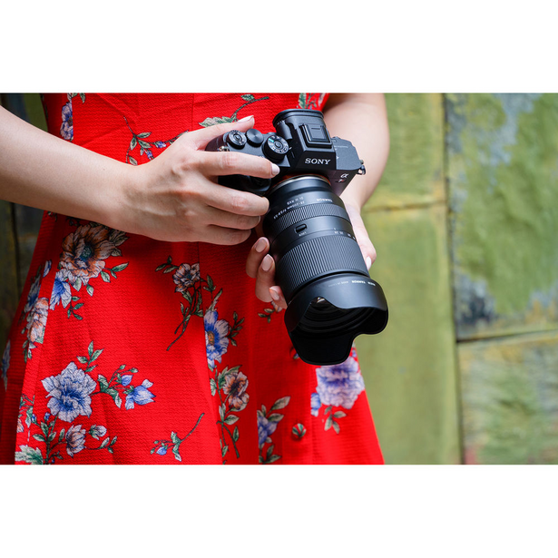 Photographer in red floral dress holding mirrorless camera with telephoto lens