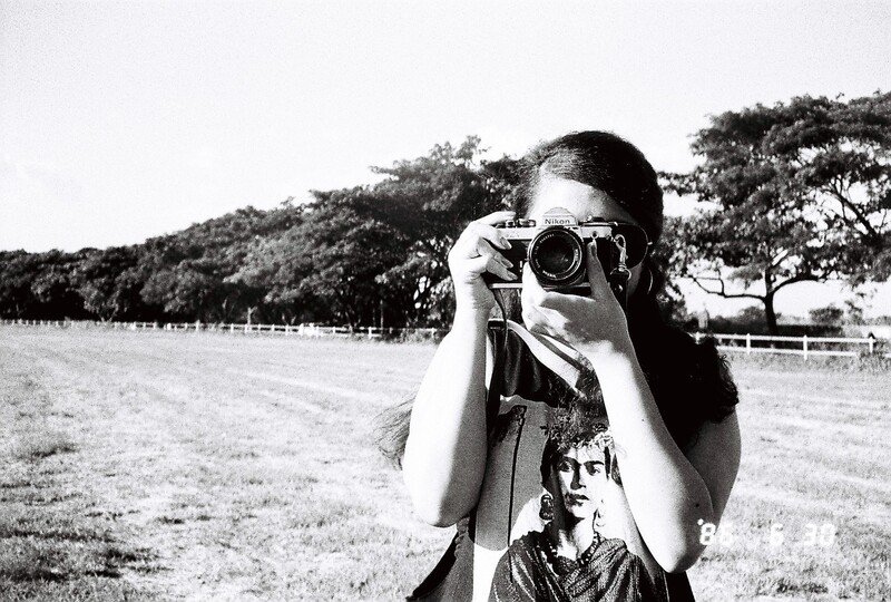 Photographer holding vintage SLR camera to face in open field landscape