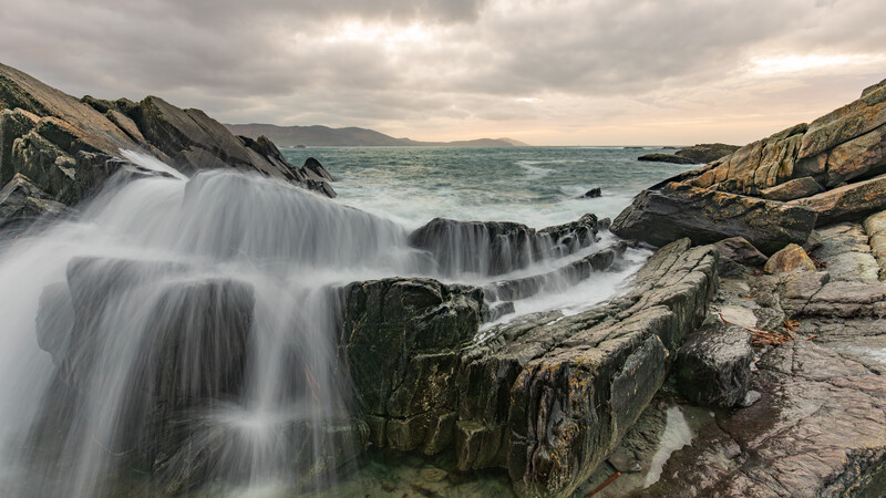 Coastal waves crashing over stratified rock formations with long exposure blur effect