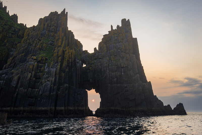Dramatic basalt sea stacks silhouetted against golden sunset over calm ocean waters