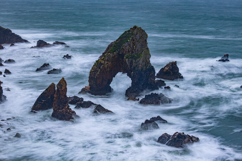 Dramatic coastal rock formations with natural arch surrounded by crashing waves