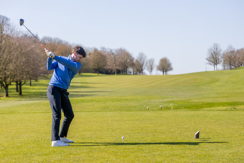 Golfer mid-swing on bright fairway with bare trees and manicured course in background