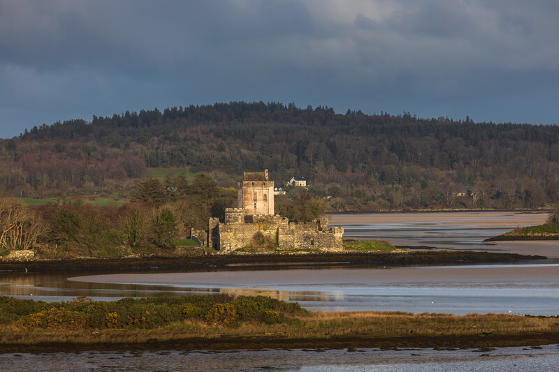 Medieval castle on a peninsula surrounded by water with forested hills in the background