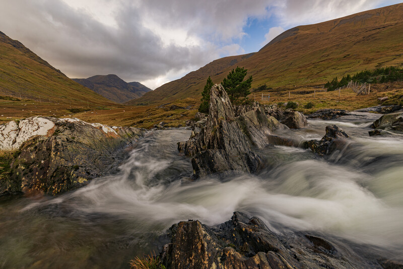 Mountain river with long exposure flowing past dark rocky outcrops in Scottish Highlands valley