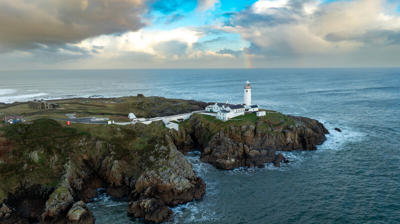 Lighthouse on rocky headland overlooking dramatic coastal cliffs and ocean under dramatic sky