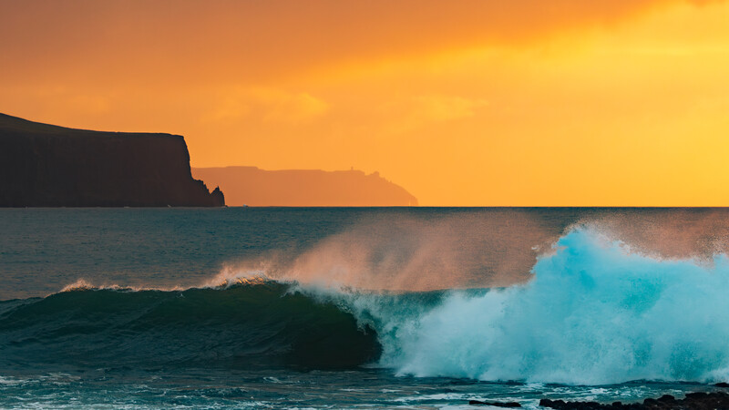 Turquoise wave breaking at sunset with silhouetted cliffs