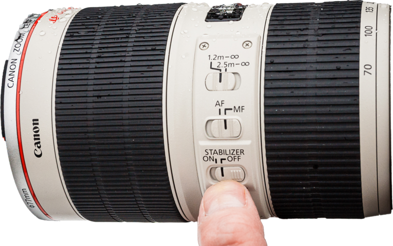 Canon telephoto lens with stabilizer and autofocus controls visible, finger demonstrating stabilizer toggle switch