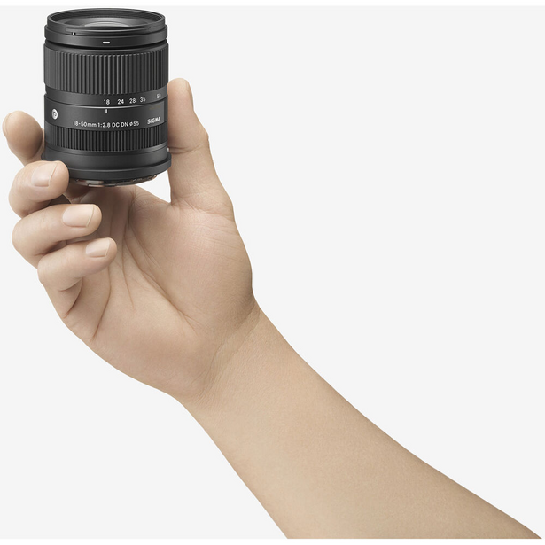 Hand holding a black telephoto zoom lens with focus ring and distance scale visible