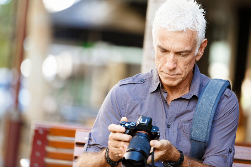 Mature male photographer examining DSLR camera outdoors