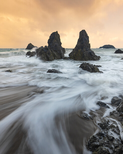Dramatic rocky sea stacks rising from turbulent waves at golden hour