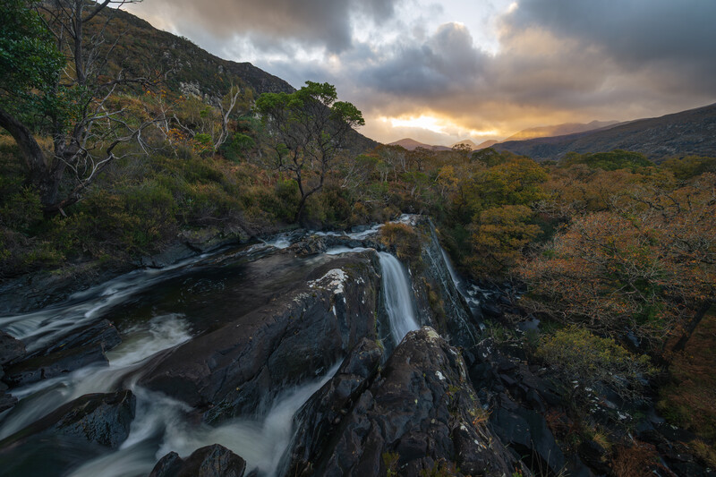 Cascading waterfall flowing over dark rocks with misty long exposure effect in Scottish highlands landscape