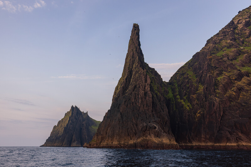 Dramatic basalt sea stacks rising from calm ocean waters with moss-covered slopes