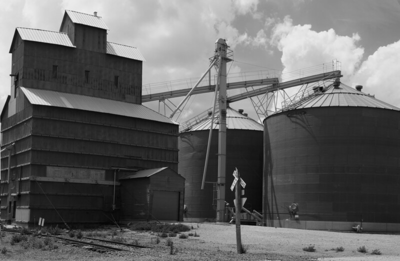 Black and white photograph of industrial grain storage facility with elevator tower and metal silos