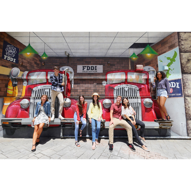 Five people seated on red vintage car props in front of an oversized FDDI storefront display