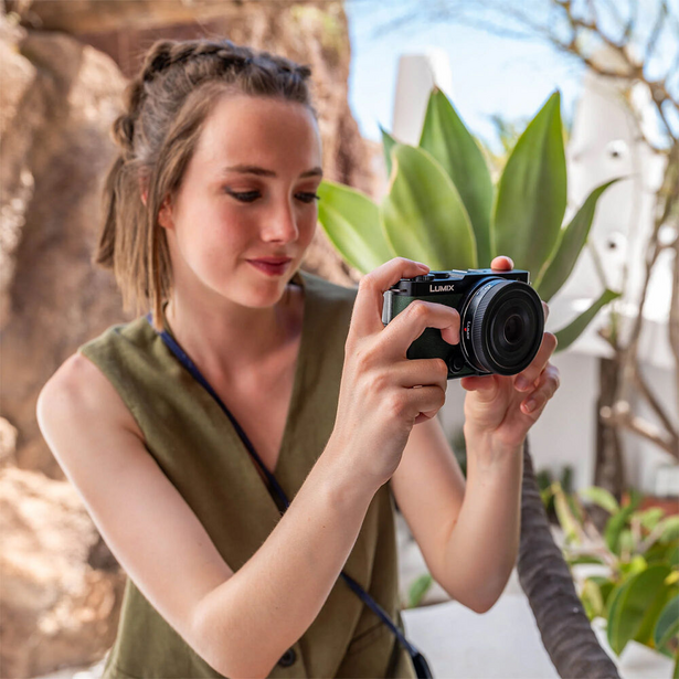 Female photographer holding a compact digital camera, composing a shot with tropical plants in background