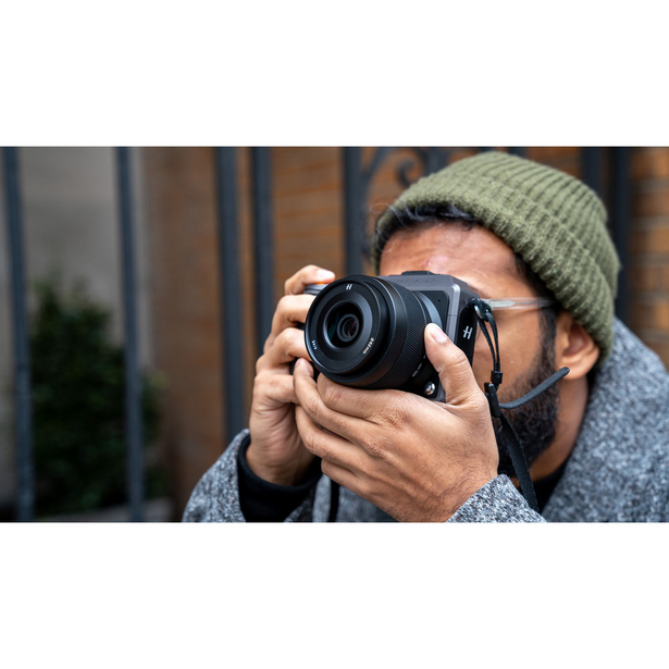 Photographer wearing glasses and beanie holding mirrorless camera to eye while shooting