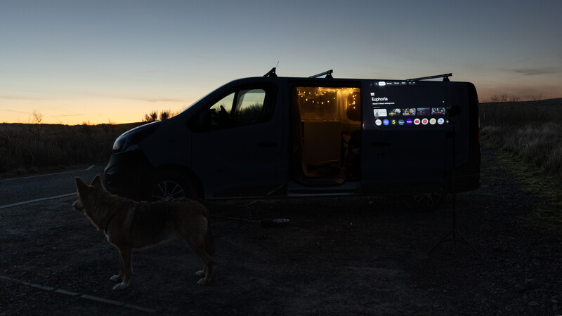 Silhouetted van with open side door and interior lighting during golden hour sunset
