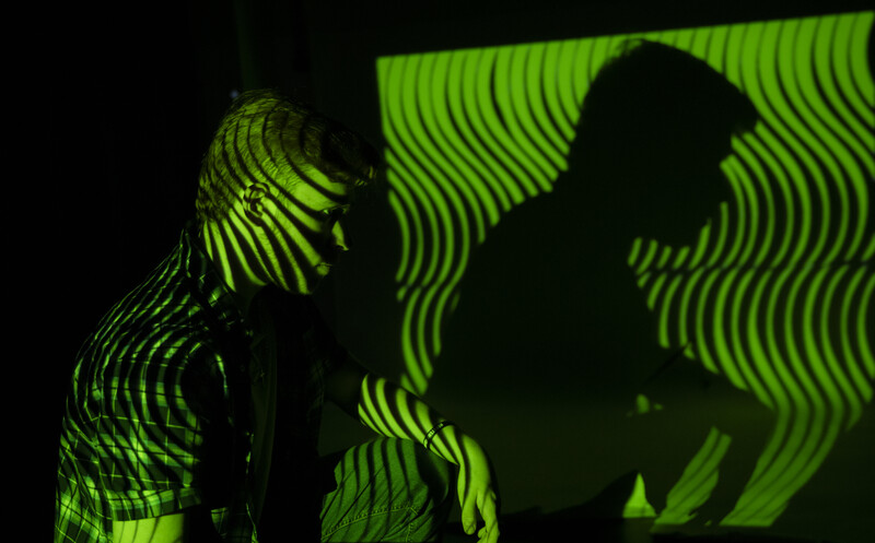 Silhouetted figure against glowing green vertical line pattern projection