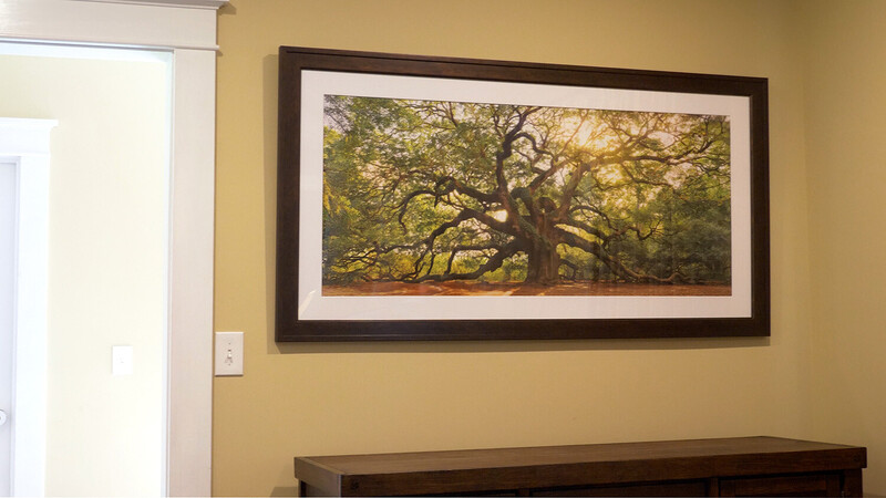 Framed landscape photograph of a large, sprawling oak tree with golden sunlit foliage displayed on mustard yellow wall