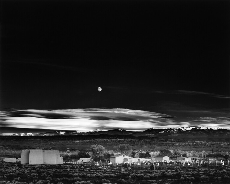 Full moon rising above a sprawling city under dramatic clouded sky, black and white