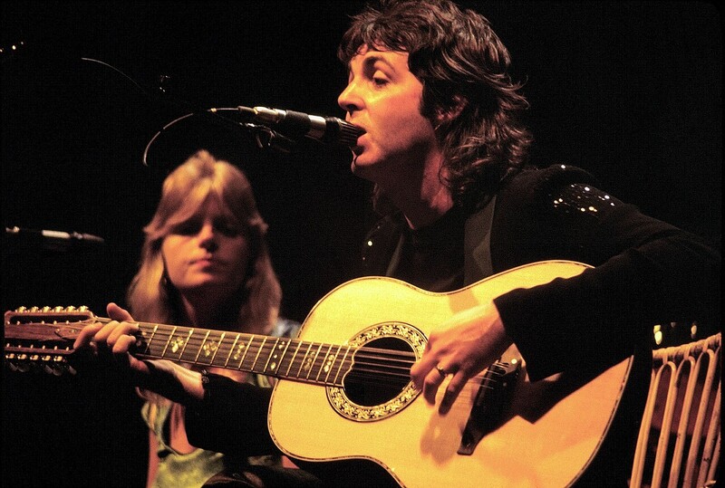 Musician performing with acoustic guitar at microphone, accompanied by guitarist in background