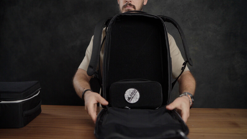 Man displaying an open black camera backpack with organizational compartments on a wooden table