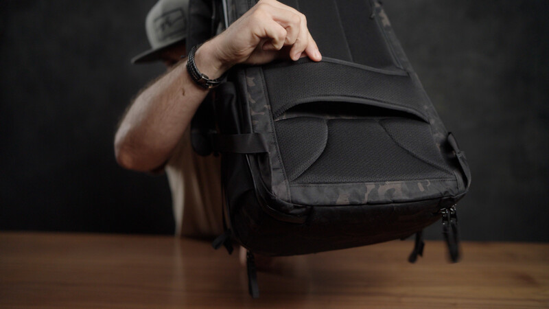 Person holding black camera bag with shoulder strap over wooden surface