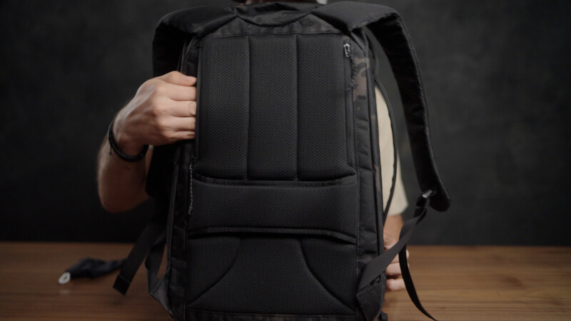 Person holding black backpack with padded compartments and shoulder straps