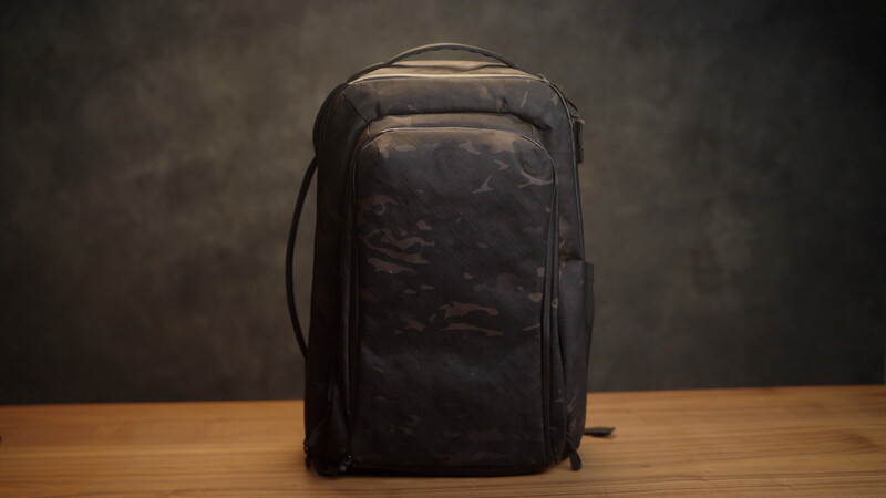 Black leather camera backpack with front pocket on wooden table against textured gray background