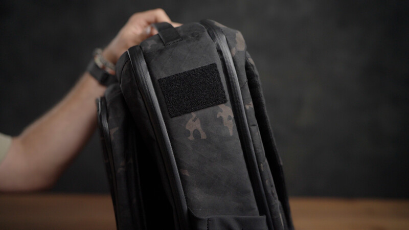 Person holding open a black tactical backpack with modular MOLLE webbing system