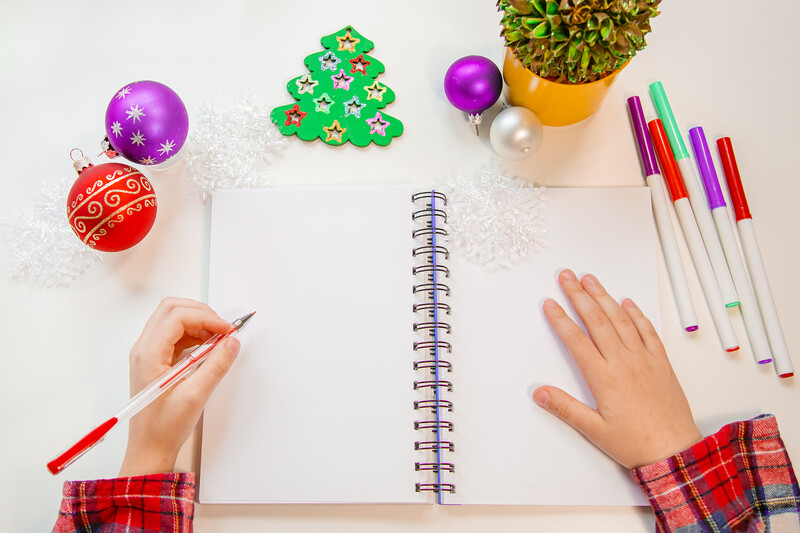 Overhead flat lay of open spiral notebook with holiday decorations and colored markers surrounding it