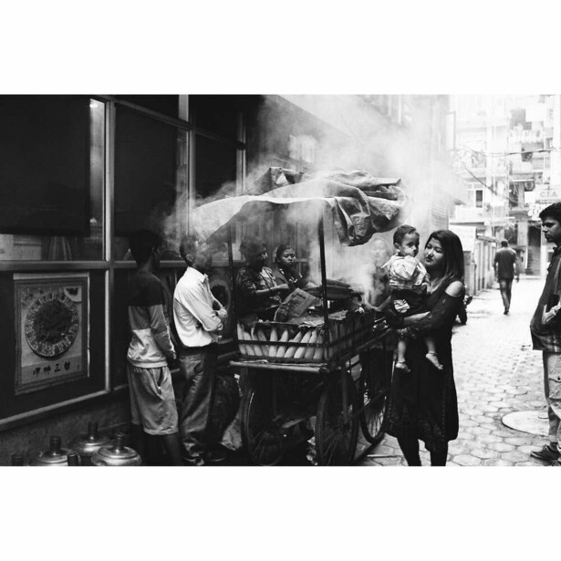 Black and white street scene showing people spraying water from a fire hose at a street vendor's cart