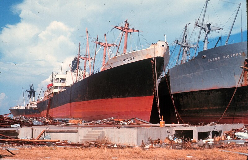 Large cargo ships beached and partially dismantled at a shipbreaking facility under blue sky