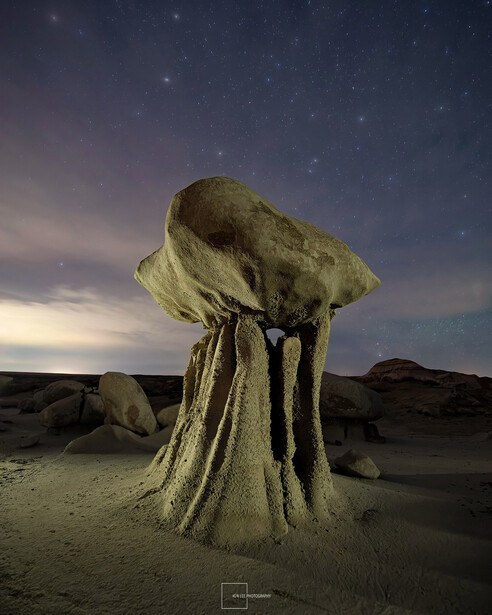 Mushroom-shaped rock formation illuminated against twilight sky with stars