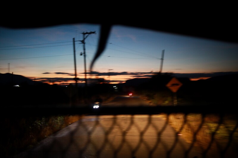 Sunset landscape with chain-link fence in sharp foreground, power lines and utility poles silhouetted against golden sky