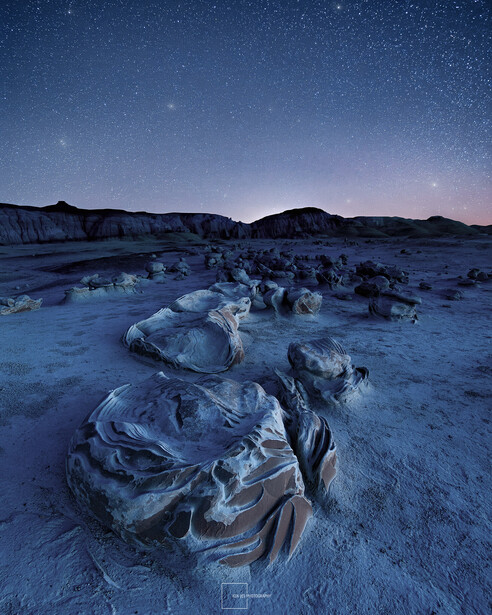 Frost-covered rocks scatter across frozen desert terrain beneath a starlit night sky