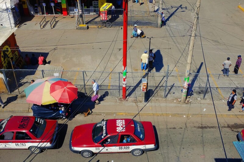 Overhead view of a street scene with red police cars, colorful umbrellas, and people scattered across a plaza