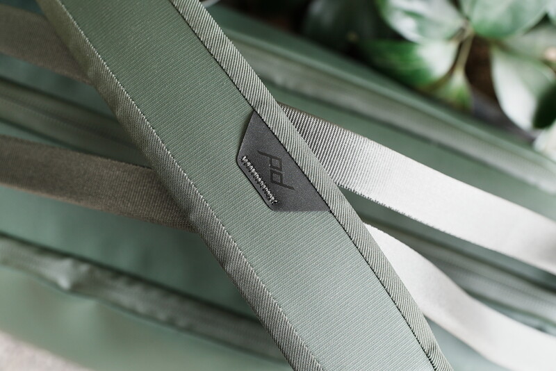 Close-up of camera strap with branded metal hardware detail against blurred green striped fabric background