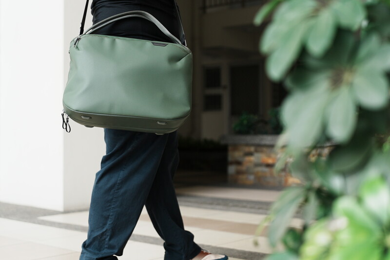 Person wearing sage green messenger bag over shoulder while standing in doorway