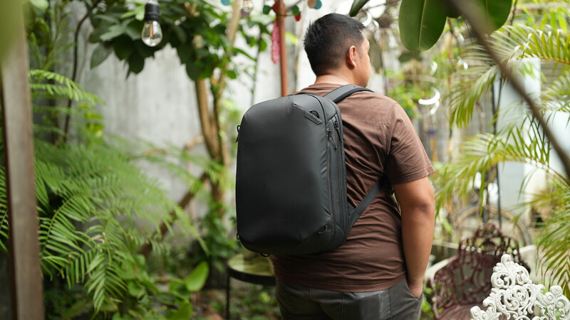 Man wearing black backpack walking through lush greenhouse with tropical plants