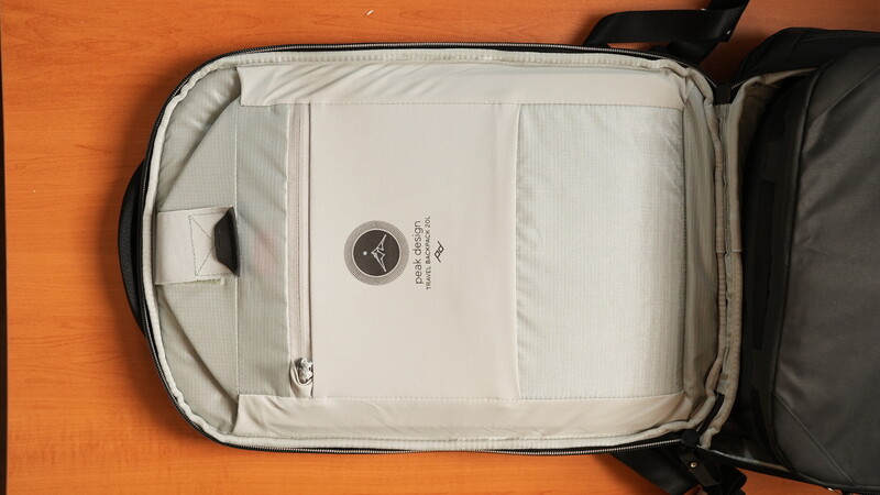 Interior view of an open camera backpack with cream-colored compartments and organizational pockets against an orange surface