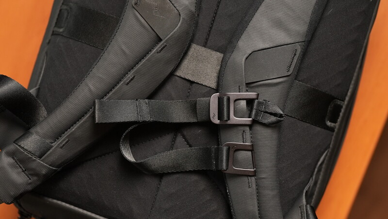 Close-up of black camera backpack straps and buckles against orange background