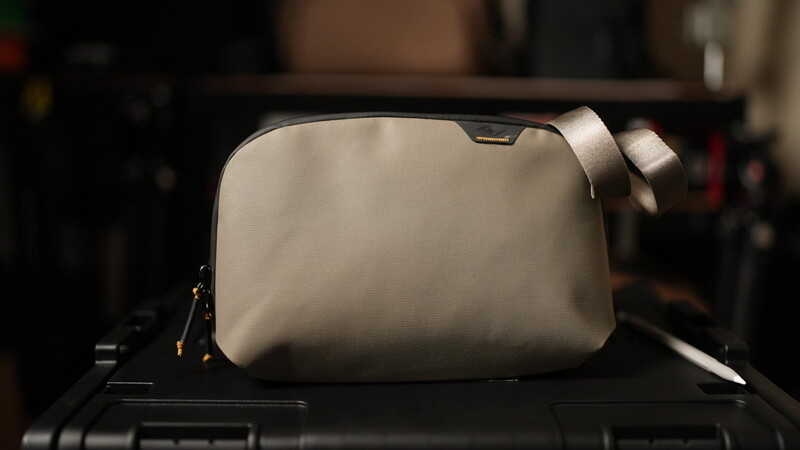 White camera bag with shoulder strap positioned on dark surface with blurred studio background