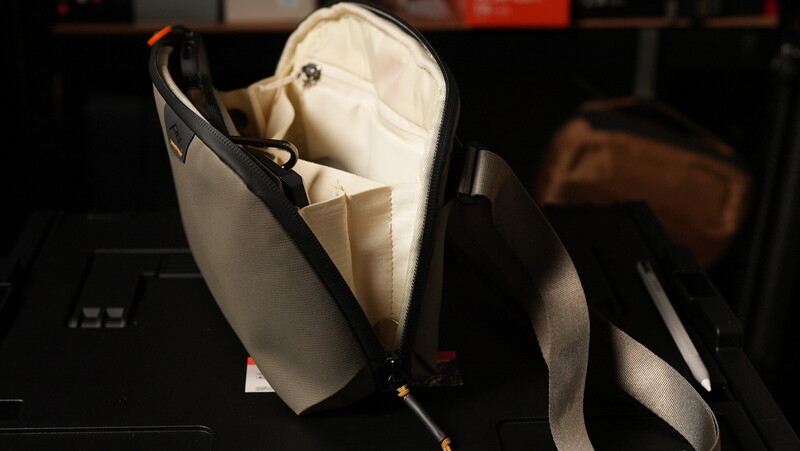 Open black camera bag with cream-colored interior lining and a white baseball cap inside