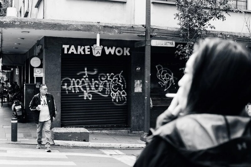Black and white street photography of a person in foreground with a shuttered storefront reading 'TAKE WOK' in the background