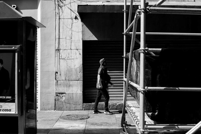 Man in dark clothing walking through urban alley with industrial architecture and scaffolding
