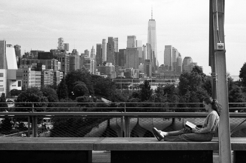 Person sitting on a bench overlooking Manhattan skyline in black and white