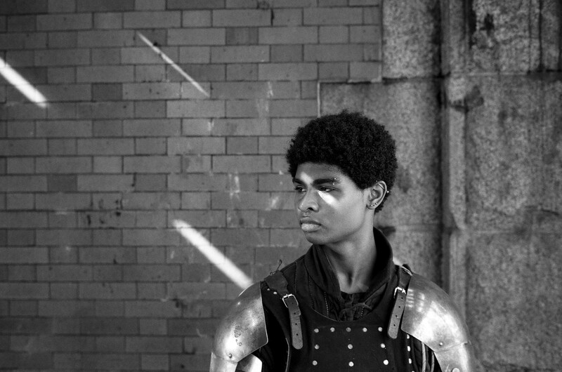 Black and white portrait of a young man against brick wall with dramatic side lighting