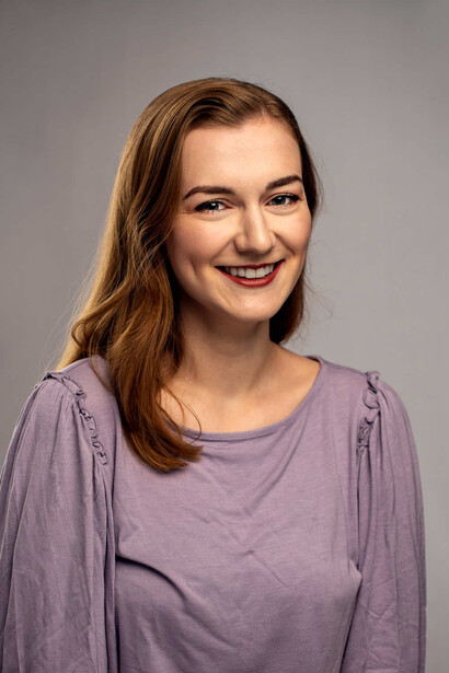 Woman with shoulder-length brown hair smiling at camera against neutral gray background